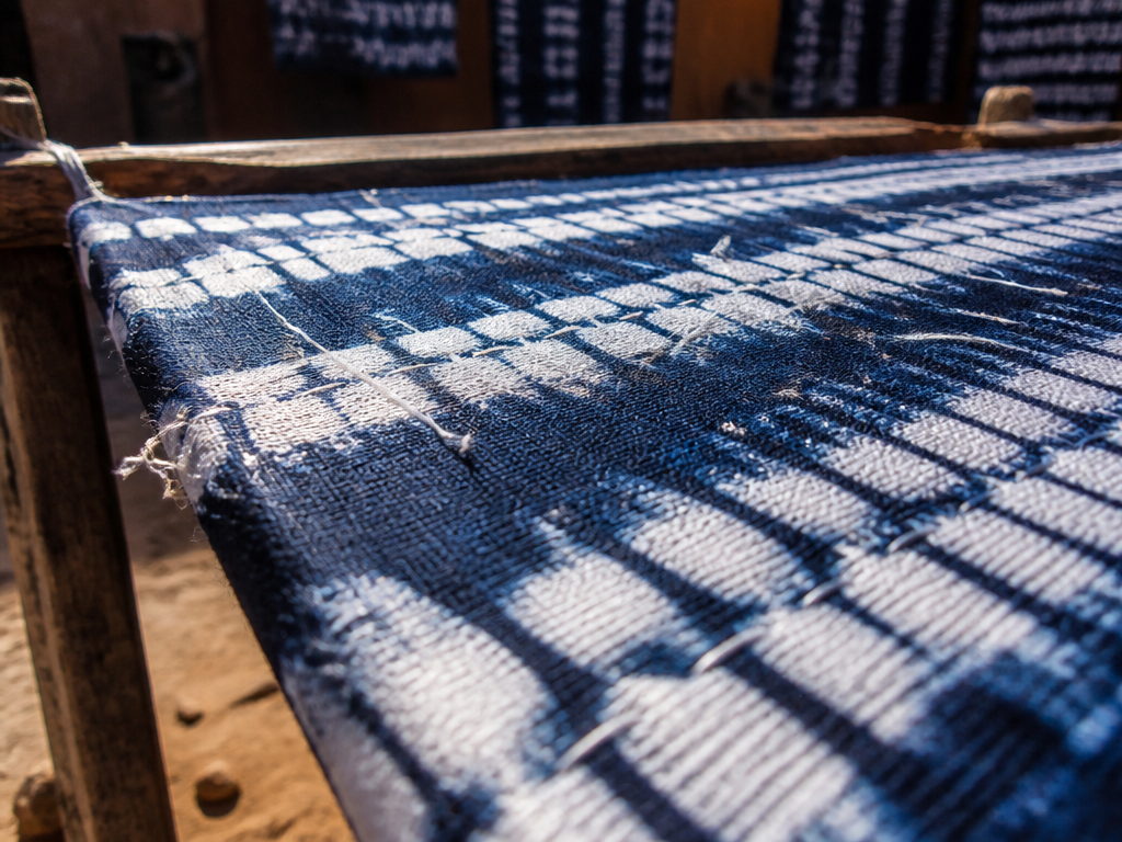 Extreme close-up photograph of a length of indigo resist-dyed adire cloth stretched taut across…