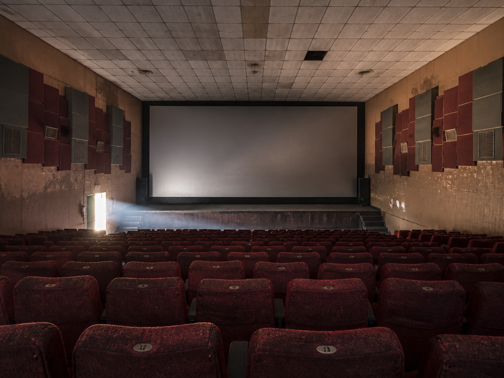 An empty single-screen cinema auditorium in West Africa photographed in the late afternoon, worn…