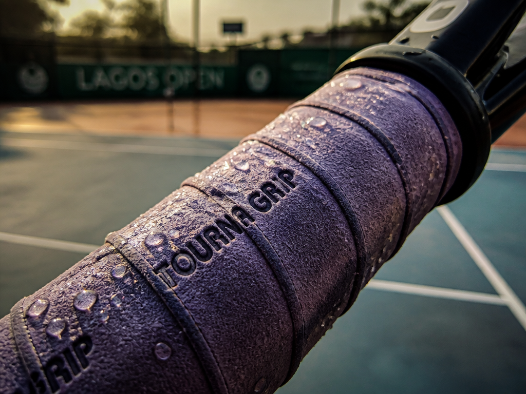 Close-up macro photograph of a tennis racquet handle wrapped in a wet Tourna Grip…