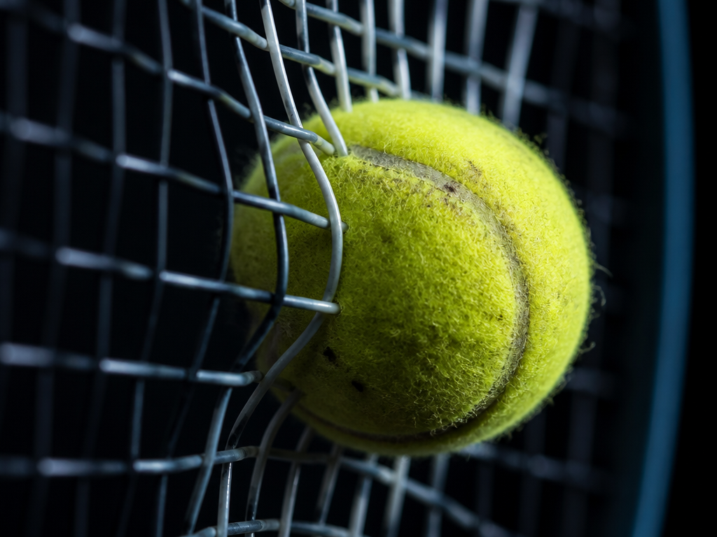 A tight macro shot of a tennis ball mid-compression against a stringbed during a…