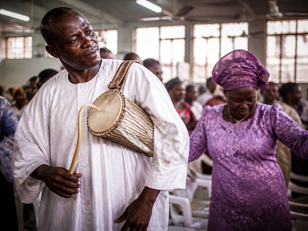 Photorealistic documentary photograph inside a Pentecostal church hall in Ibadan during a morning praise…