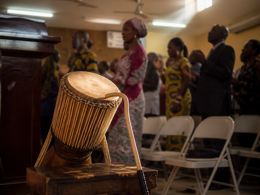 A professional documentary photograph taken inside a warm, crowded church hall during a praise-and-worship…